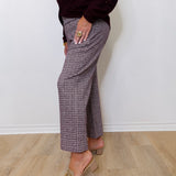 Person wearing a dark top and patterned pants against a white wall.