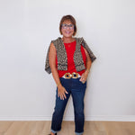 Woman wearing a red top, leopard print vest, blue jeans, and black shoes against a white wall.
