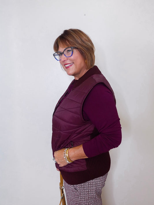 Woman wearing a purple vest over a long-sleeve shirt against a white background