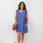 Woman wearing a blue dress with ruffled sleeves against a white wall.