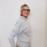 Woman wearing a gray outfit against a white wall