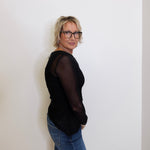 Person wearing a black top and blue jeans against a white wall