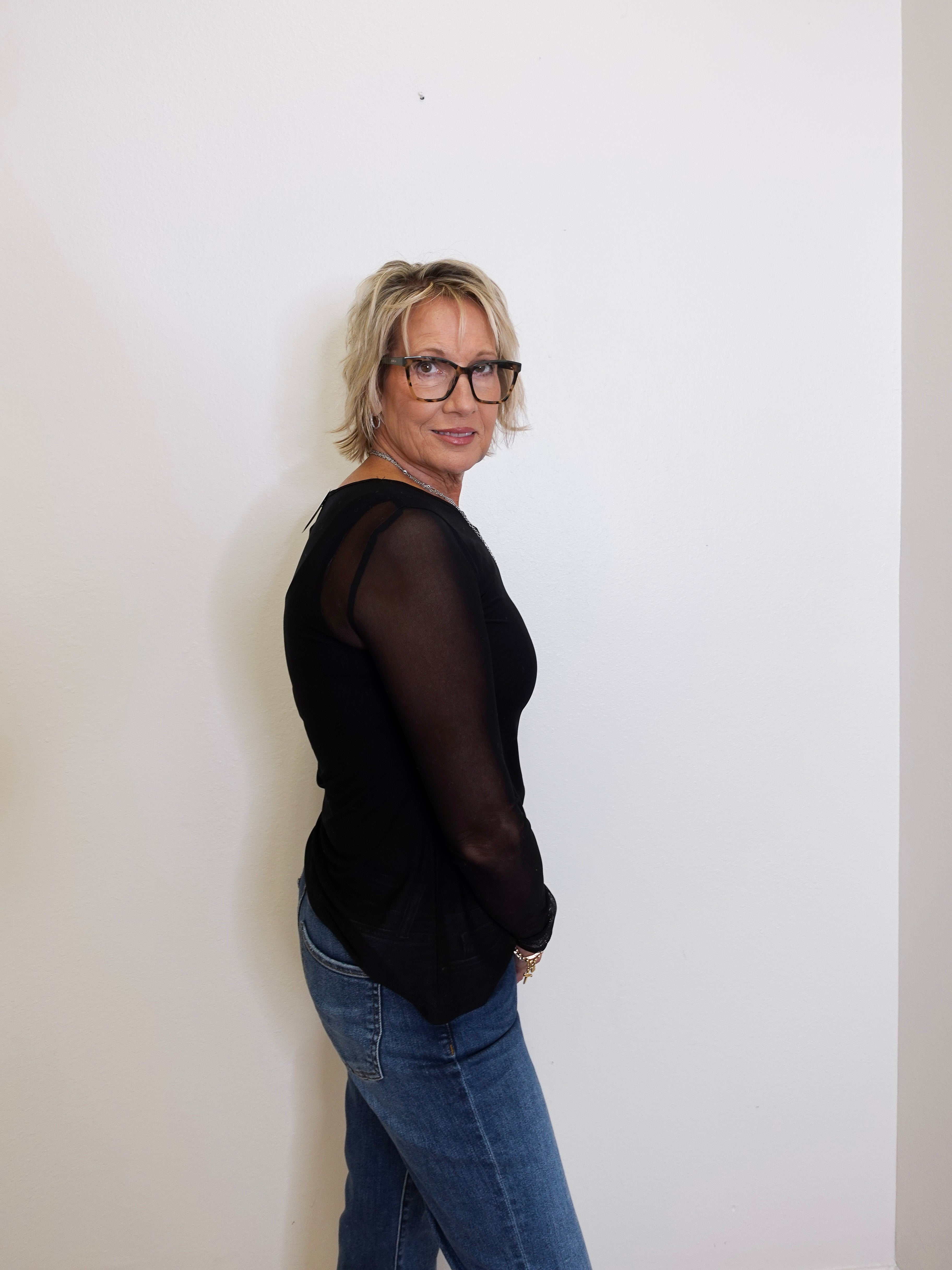 Person wearing a black top and blue jeans against a white wall