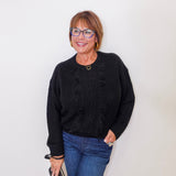 Woman wearing a black sweater and blue jeans against a white background