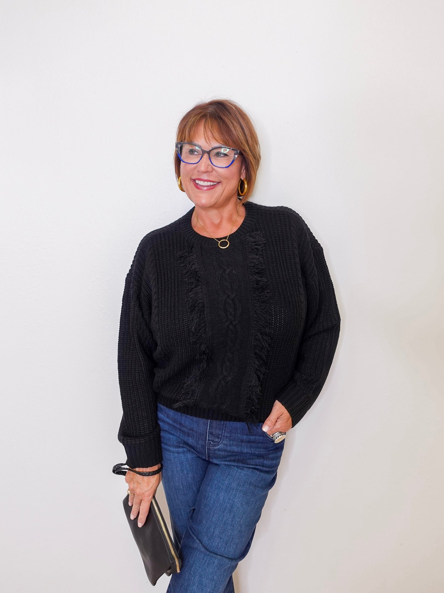 Woman wearing a black sweater and blue jeans against a white background