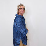 Person wearing a blue floral jacket against a white wall