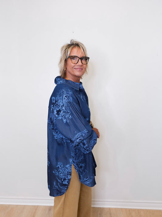 Person wearing a blue floral jacket against a white wall