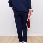 Person wearing a navy outfit holding a red handbag against a white wall.
