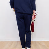 Person wearing a navy outfit holding a red handbag against a white wall.