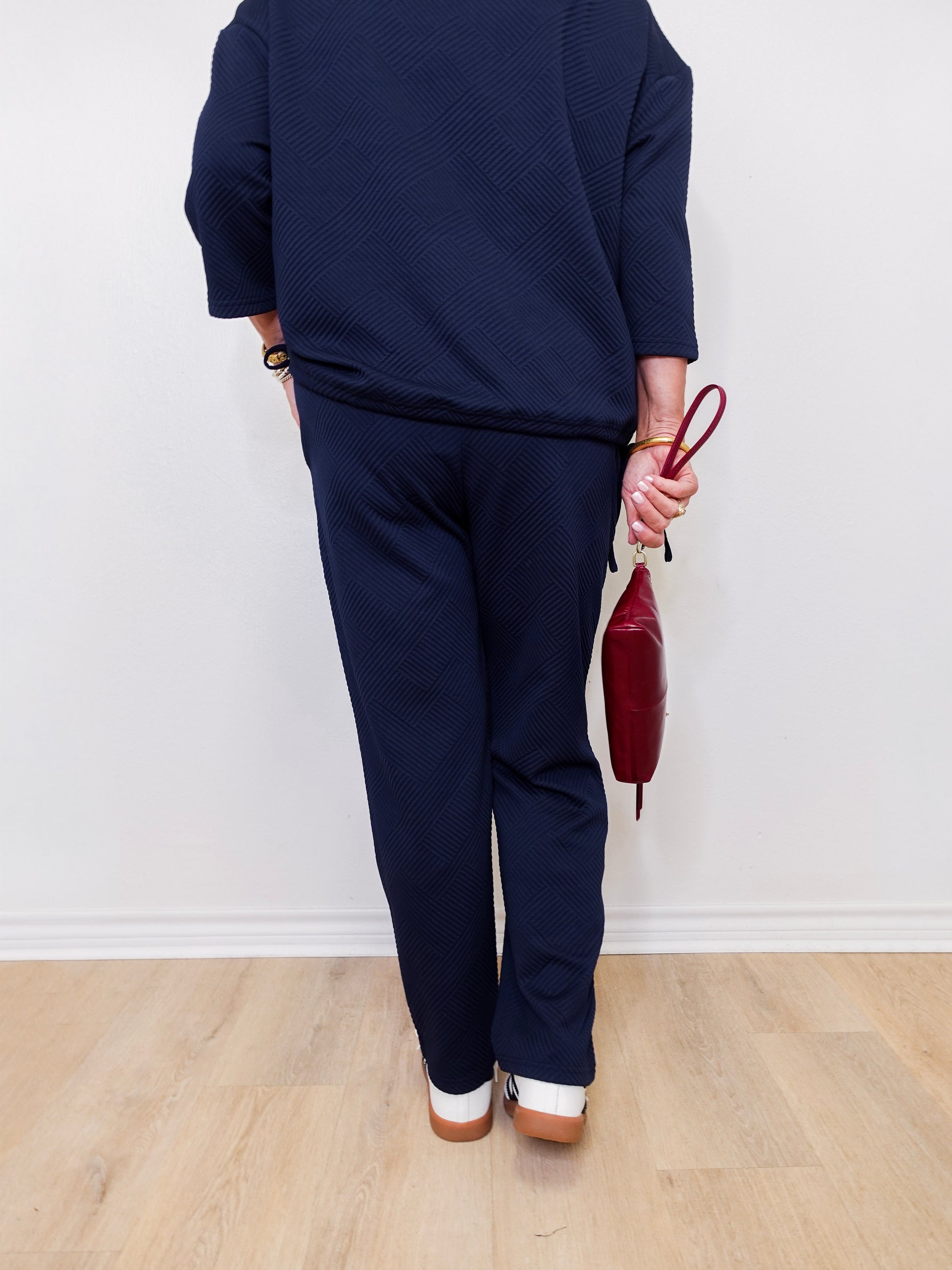 Person wearing a navy outfit holding a red handbag against a white wall.