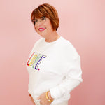 Person wearing a white sweatshirt with colorful 'LOVE' text on a pink background