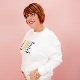 Person wearing a white sweatshirt with colorful 'LOVE' text on a pink background