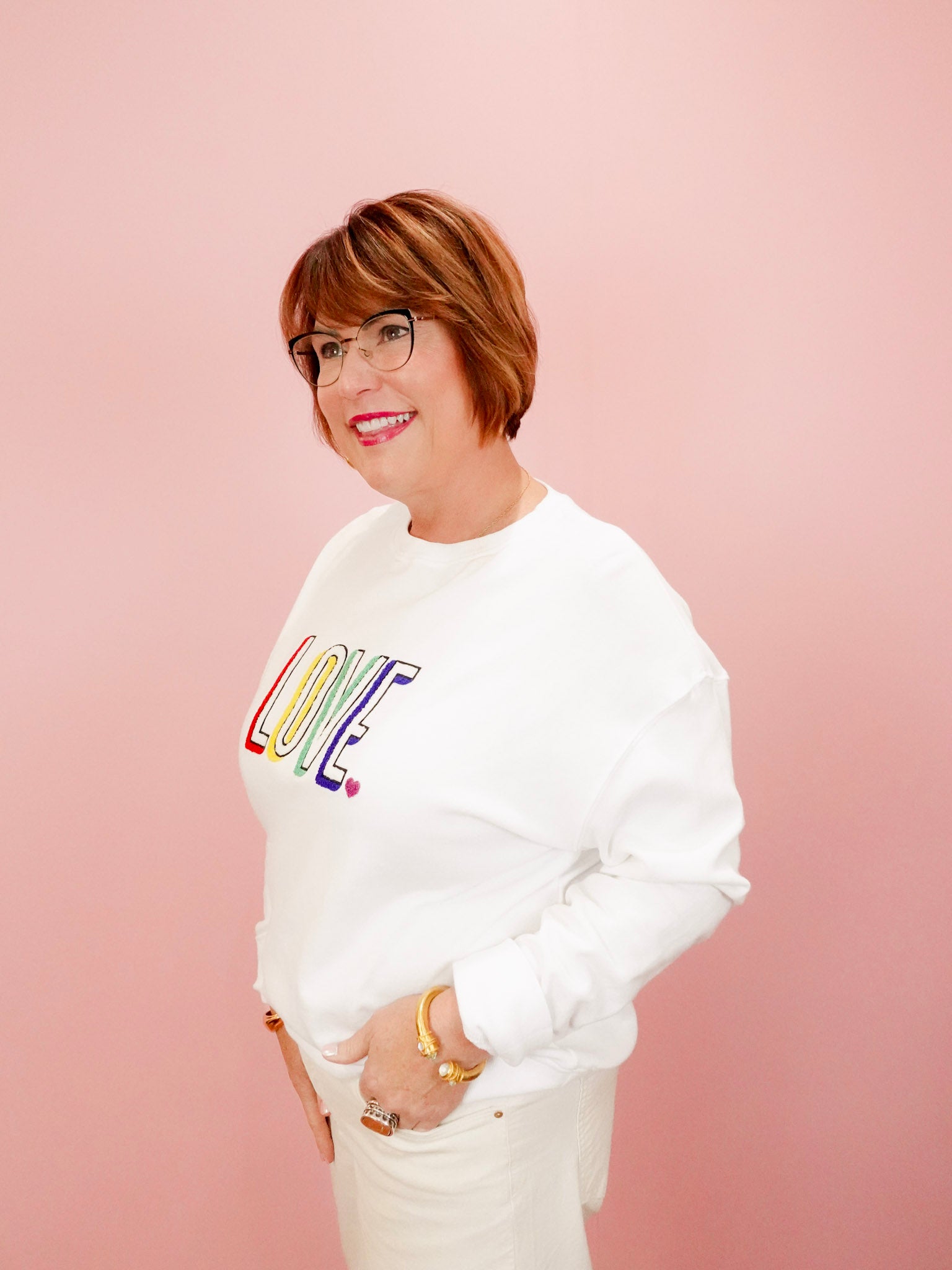 Person wearing a white sweatshirt with colorful 'LOVE' text on a pink background