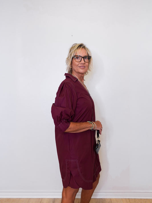 Woman wearing a burgundy dress against a white wall