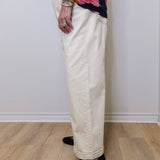 Person wearing a floral top, beige pants, and black shoes on a plain background