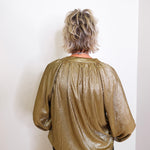 Person wearing a gold metallic blouse against a white wall