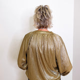 Person wearing a gold metallic blouse against a white wall