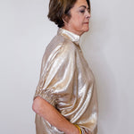 Woman wearing a shiny gold jacket against a white background