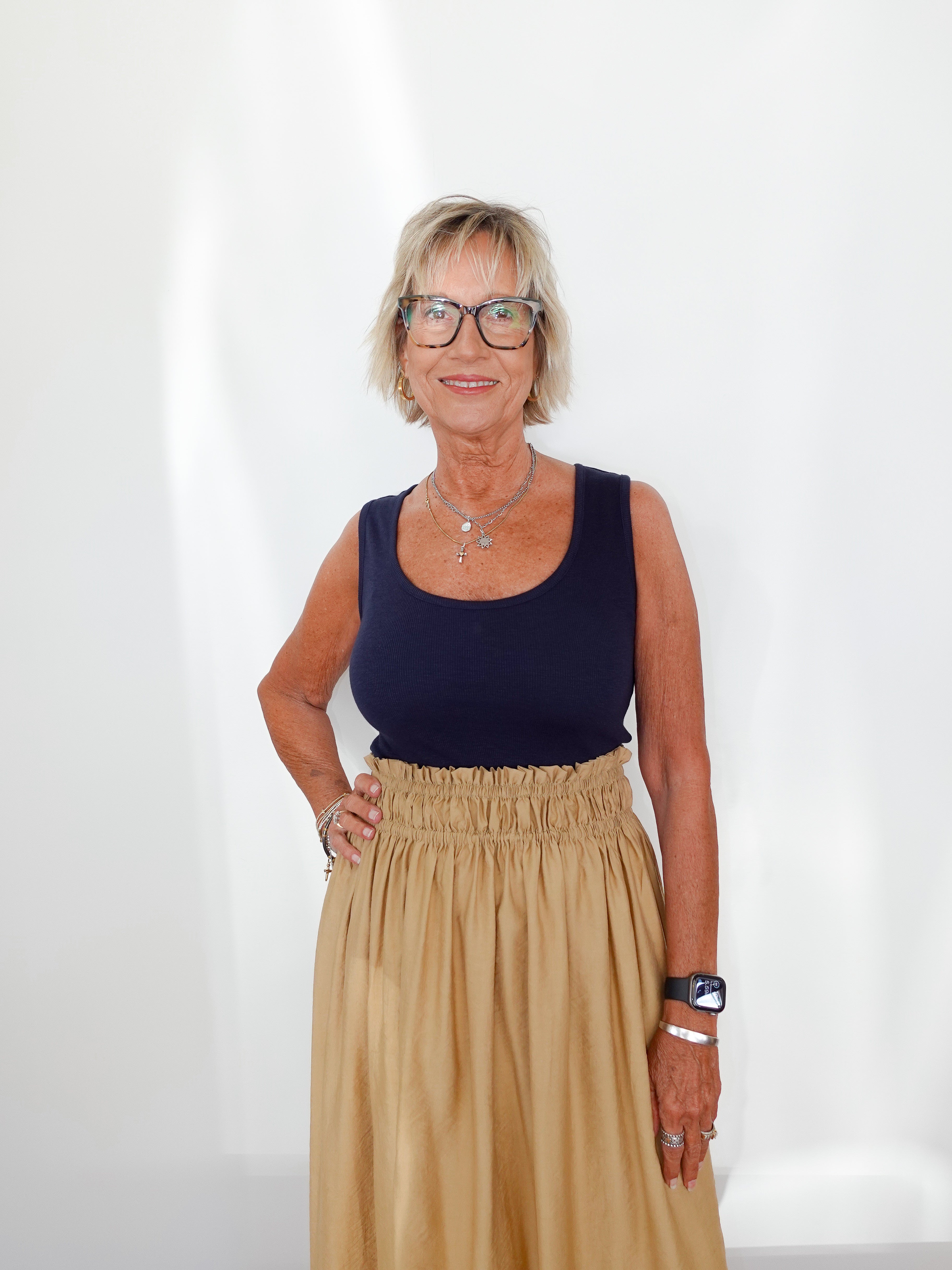 Woman wearing a navy top and beige skirt against a white background