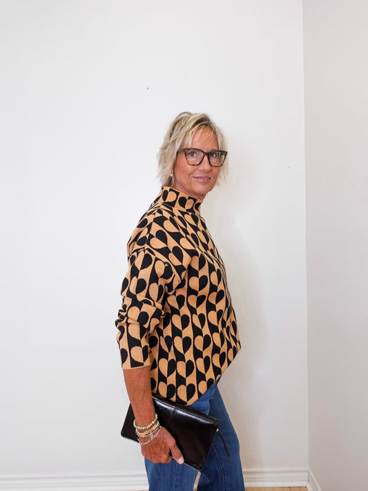 A woman modeling a mock neck heart pattern sweater in front of a white wall. 