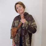 Person wearing a camouflage and leopard print jacket with a brown bag against a white background