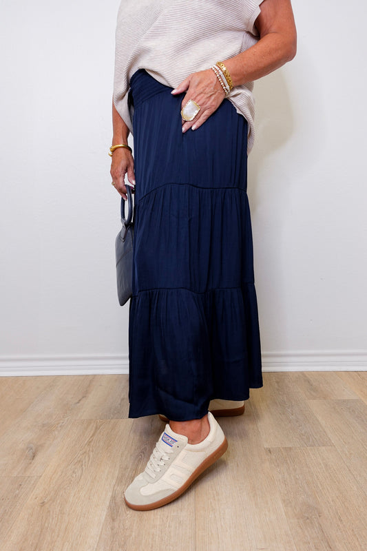 Person wearing a navy tiered skirt with white sneakers against a plain background