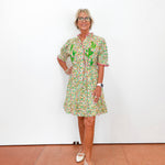Woman wearing a colorful floral dress standing against a white wall.