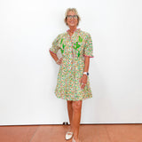 Woman wearing a colorful floral dress standing against a white wall.