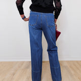 A woman modeling high rise wide leg jeans in front of a white wall. 