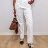 Person wearing a striped sweater, white jeans, and brown shoes, holding a brown bag against a plain background.