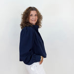 Woman wearing a navy blue blouse and white pants against a light background