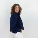 Woman wearing a navy blue blouse and white pants against a light background