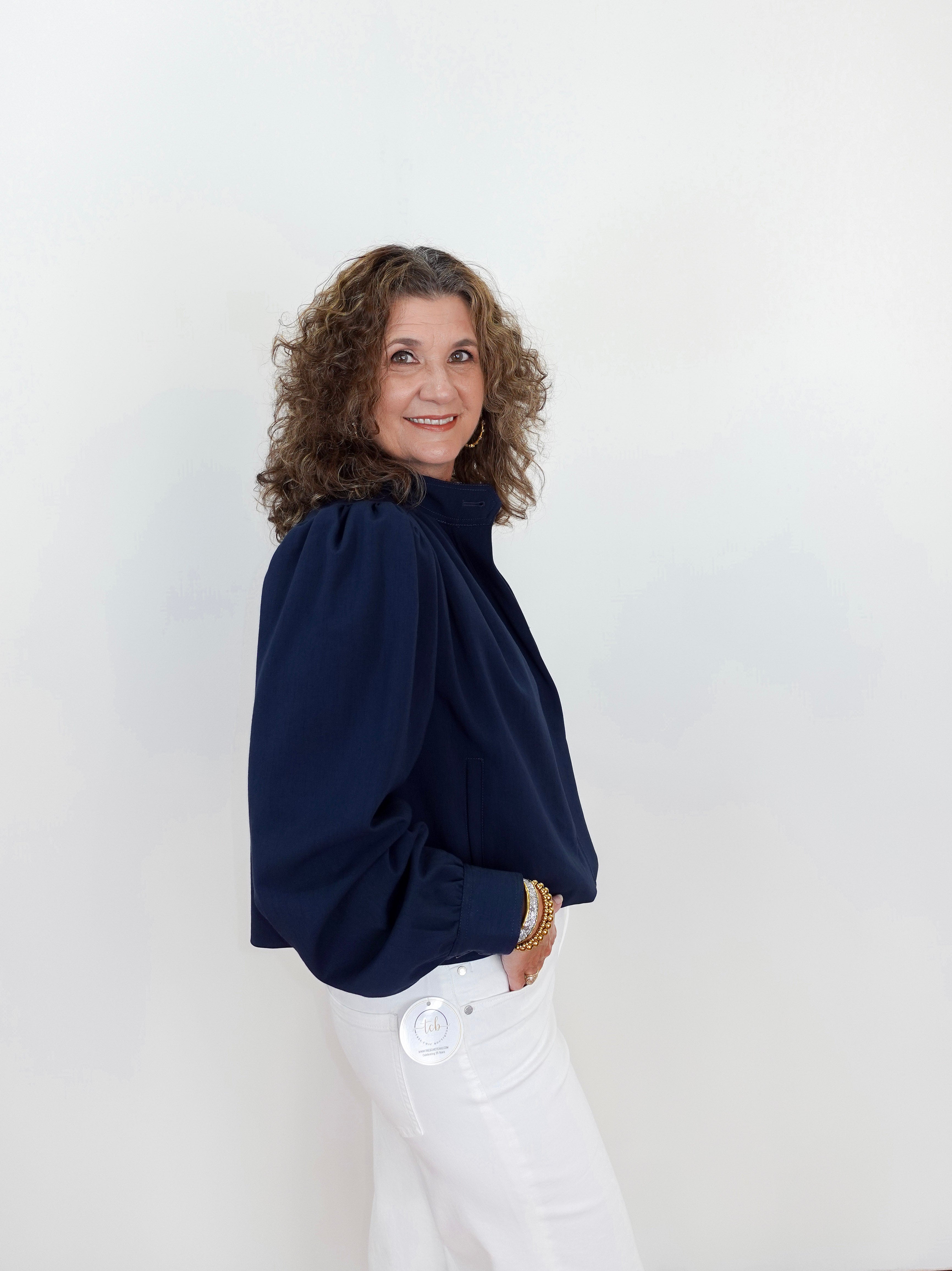 Woman wearing a navy blue blouse and white pants against a light background