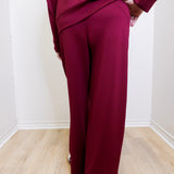 Person wearing a burgundy outfit with wide-leg pants against a white wall.