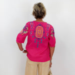 Person wearing a bright pink embroidered blouse against a white wall