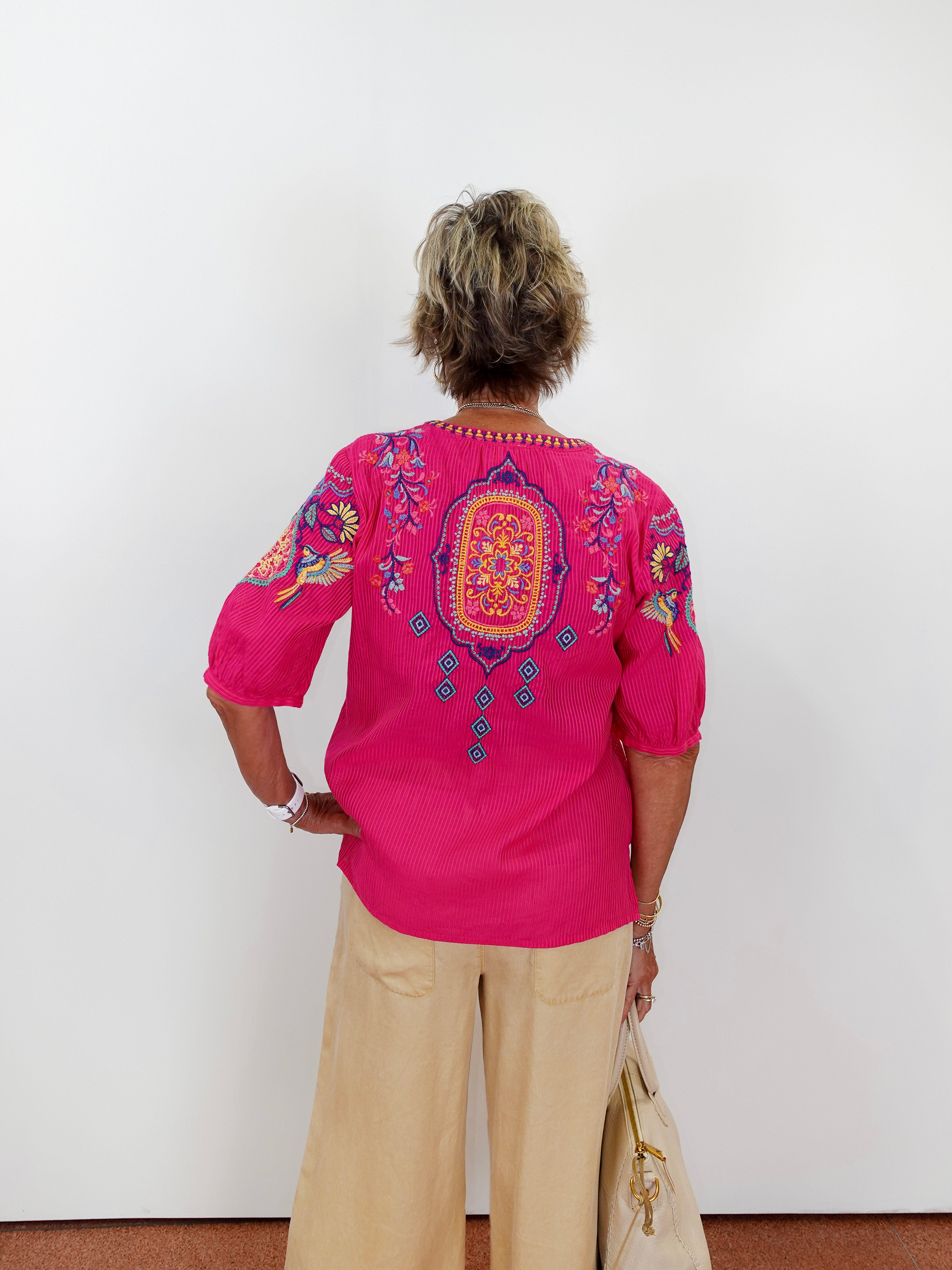 Person wearing a bright pink embroidered blouse against a white wall
