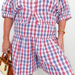 Person wearing a red, white, and blue plaid romper with a plain background
