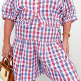 Person wearing a red, white, and blue plaid romper with a plain background