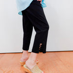 Person wearing black pants with cut-out sides, light blue top, and beige sandals on a white background.