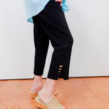 Person wearing black pants with cut-out sides, light blue top, and beige sandals on a white background.