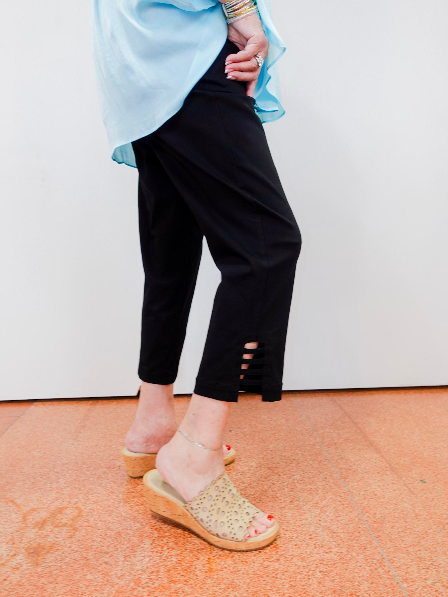 Person wearing black pants with cut-out sides, light blue top, and beige sandals on a white background.
