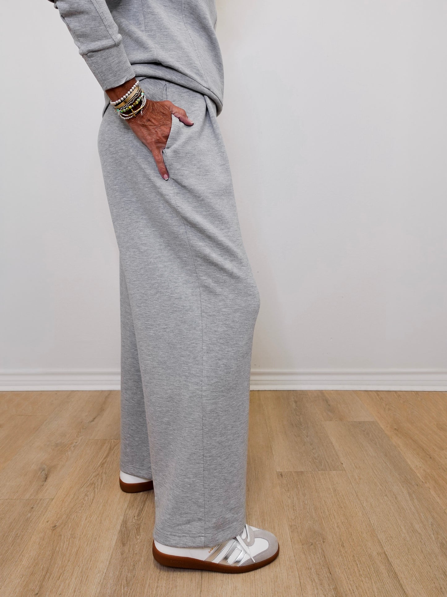 Person wearing gray sweatpants standing on a wooden floor with a white wall background
