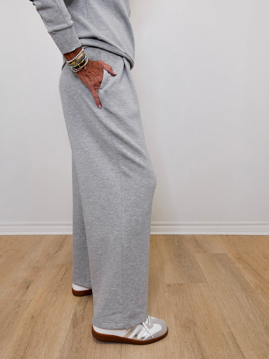 Person wearing gray sweatpants standing on a wooden floor with a white wall background