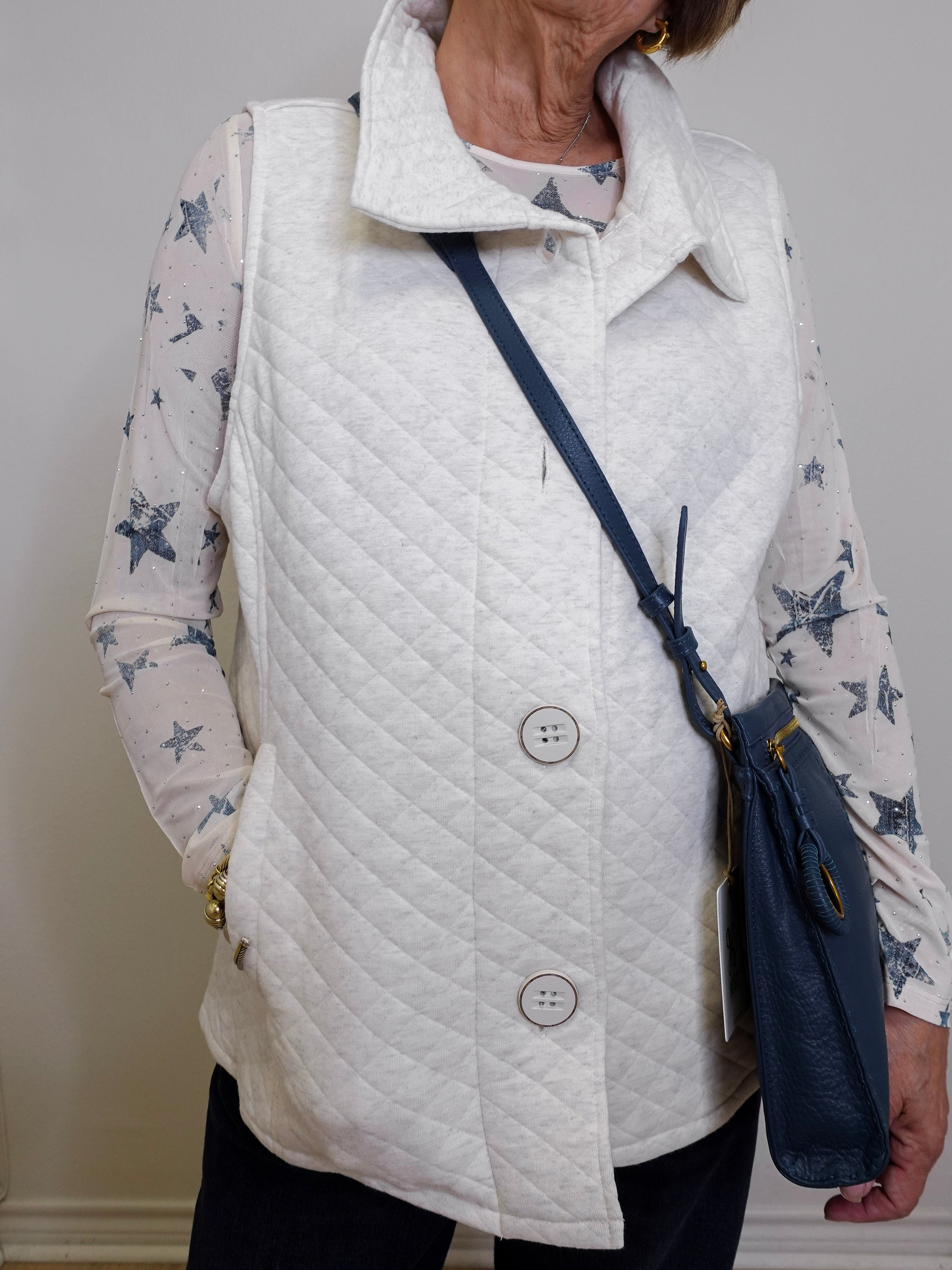 Person wearing a white quilted vest over a star-patterned shirt, holding a navy blue handbag.