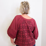 Person wearing a maroon top with geometric pattern against a white wall