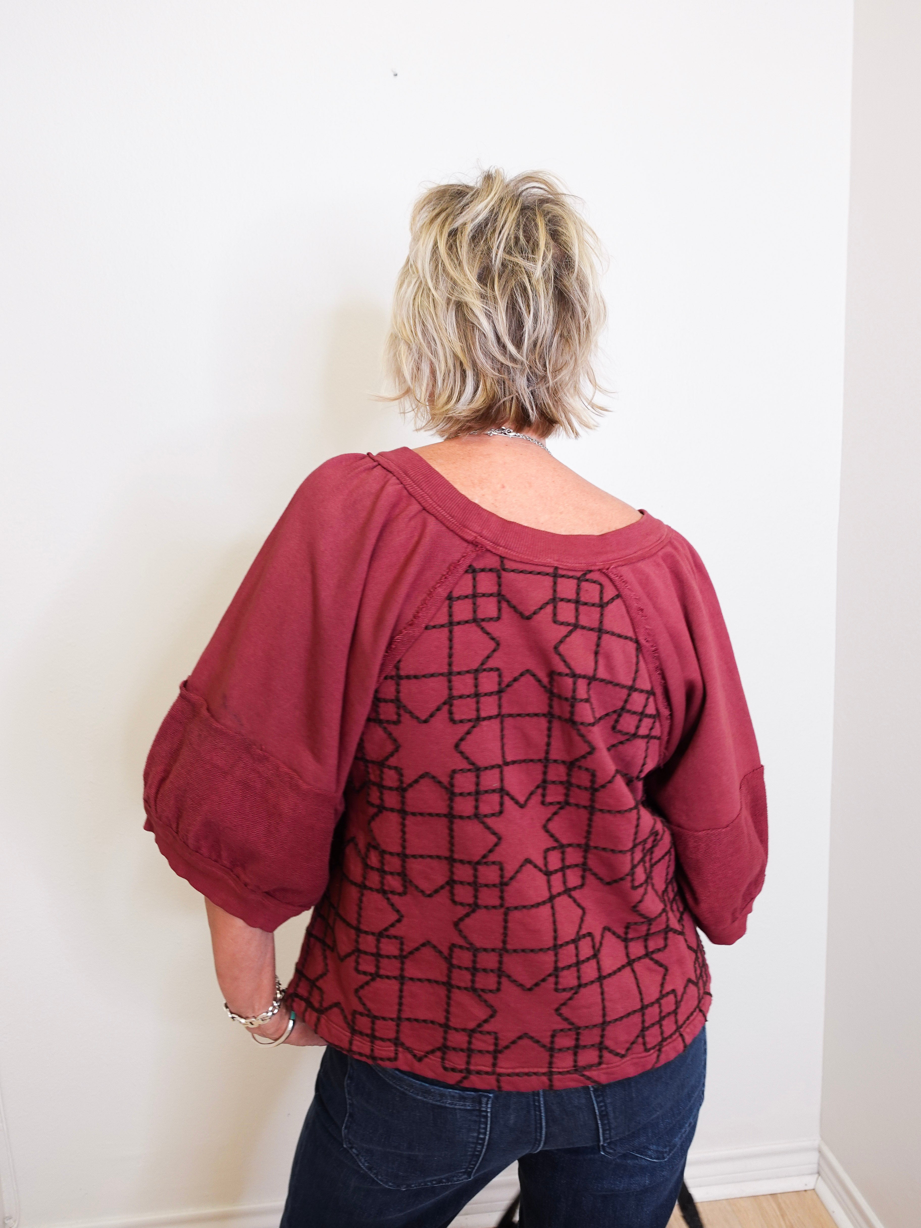 Person wearing a maroon top with geometric pattern against a white wall