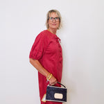 Woman in a red dress holding a black handbag against a white wall