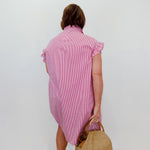 Woman wearing a pink dress holding a straw bag against a white wall