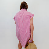 Woman wearing a pink dress holding a straw bag against a white wall