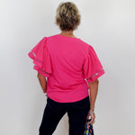 Person wearing a bright pink blouse with sheer sleeves against a white wall.